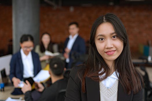 Portrait of a confident Asian businesswoman smiling in a modern office with colleagues in the background.